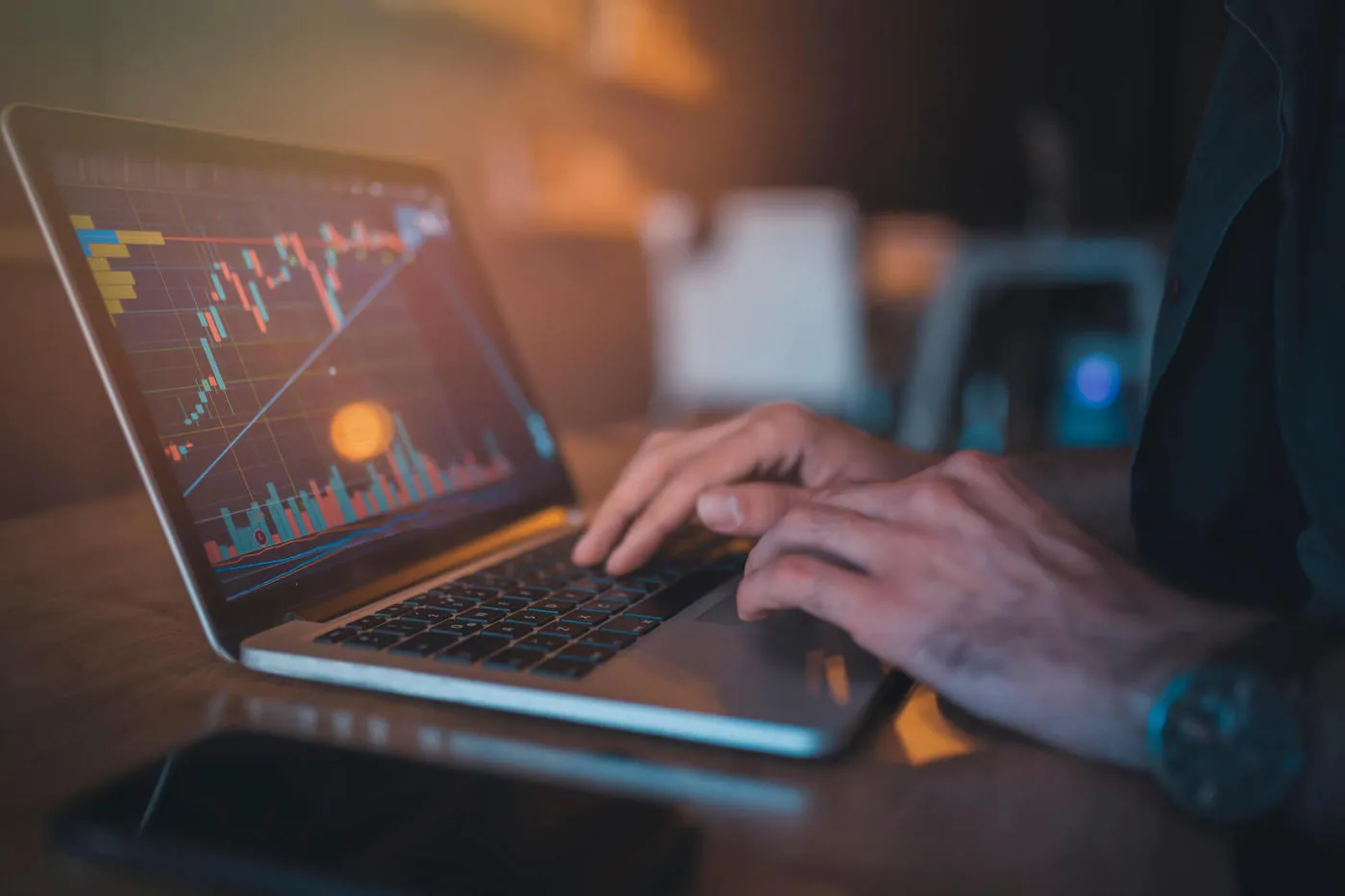 A man wearing a watch is looking at a stock chart on his laptop.