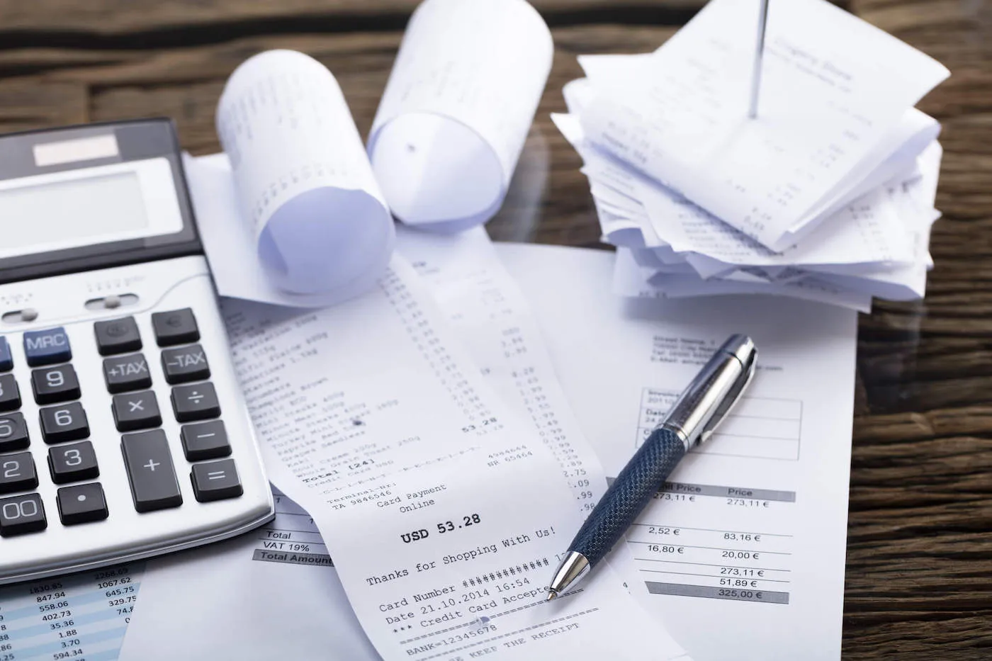 A pile of receipts with a calculator and pen on the table.