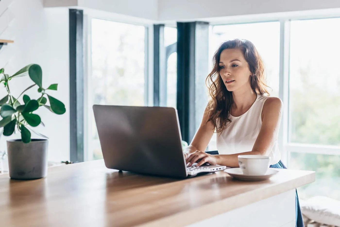 A woman types on her laptop with a teacup next to her computer.