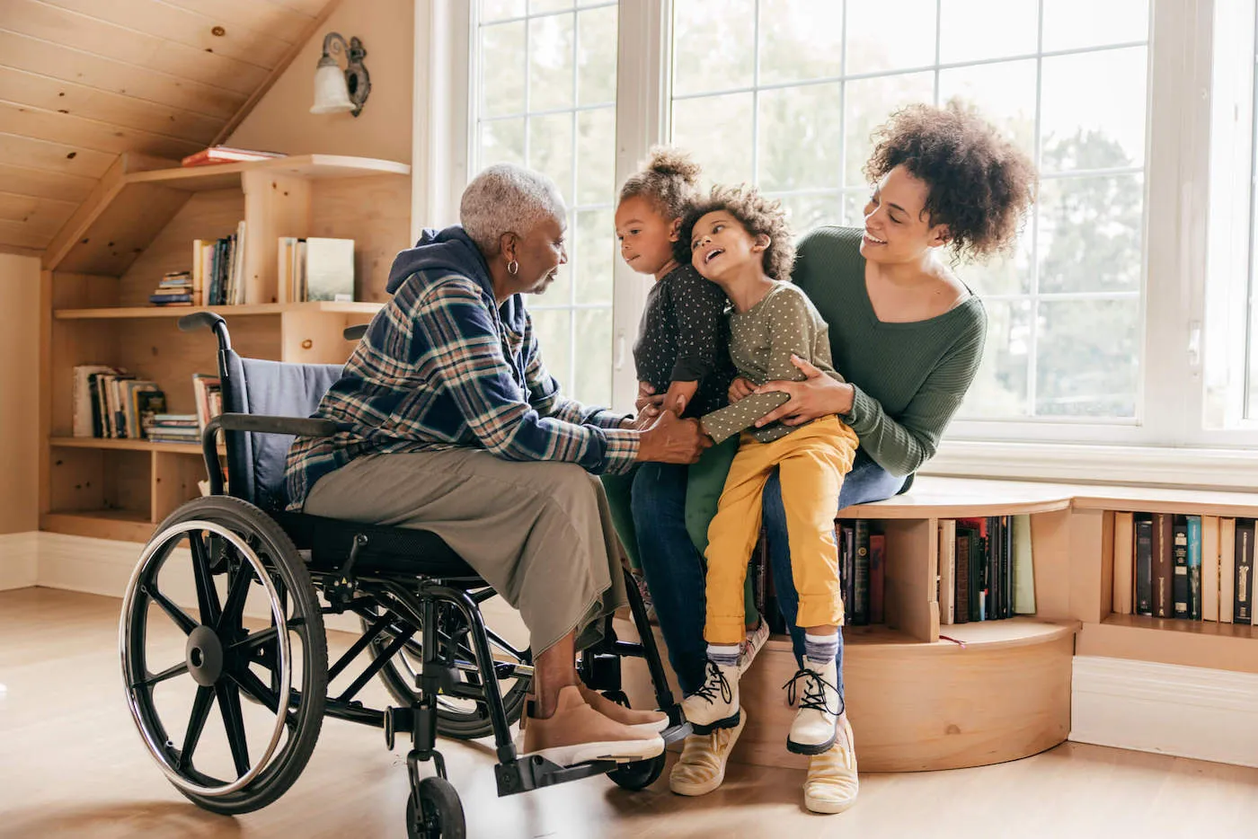 A grandmother in a wheelchair talks with her two granddaughters as their mother holds them.