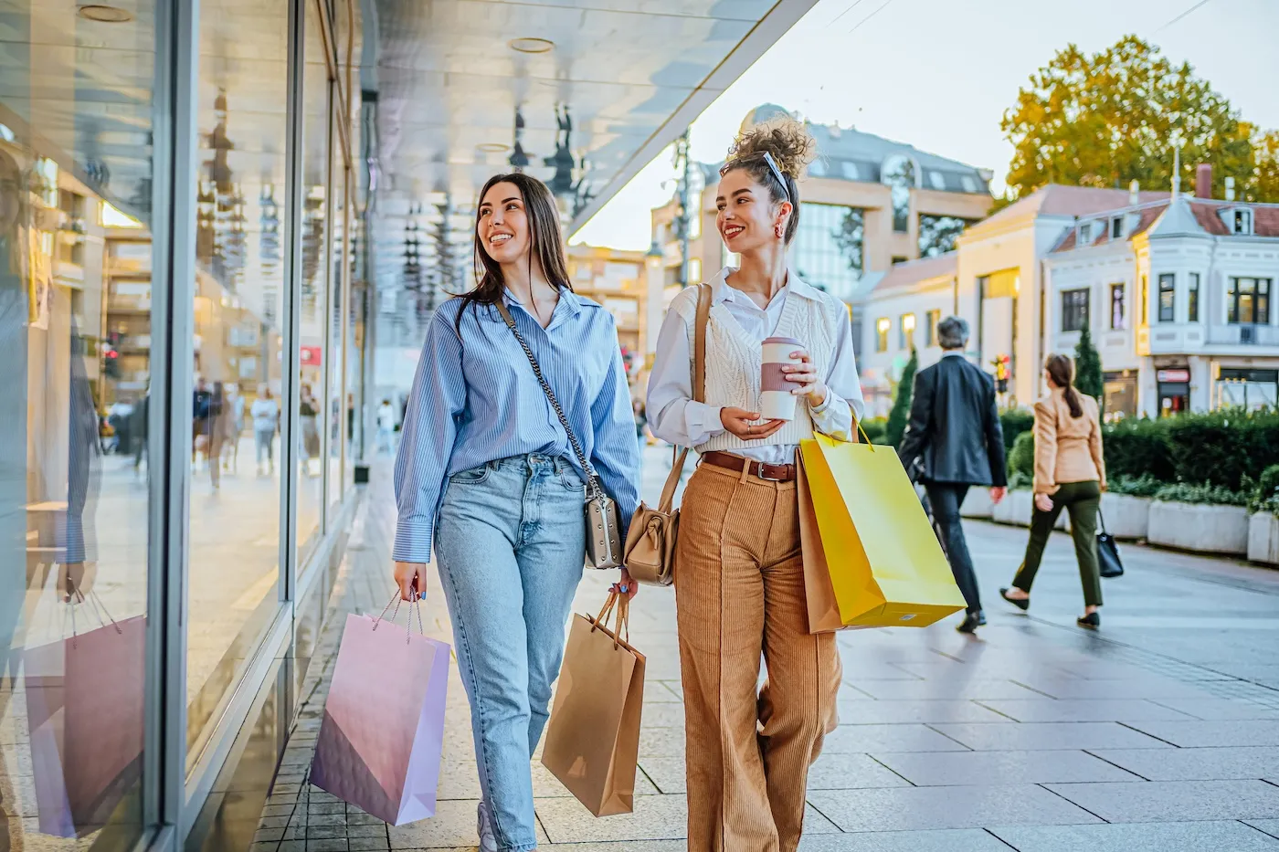 Young cheerful female friends looking at store windows while shopping together in the city.