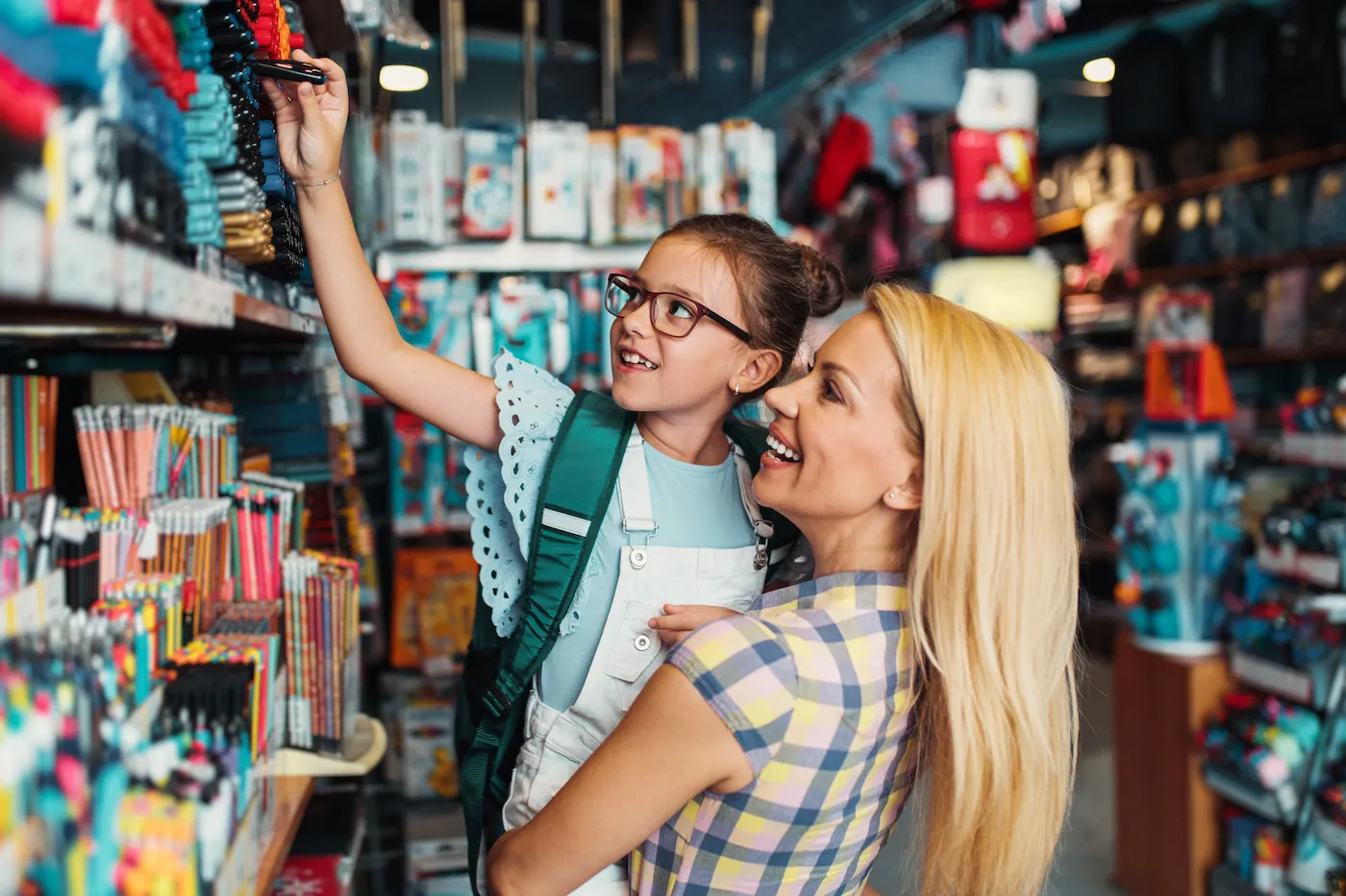 Happy mother with her daughter choosing and buying school supplies in a bookstore.