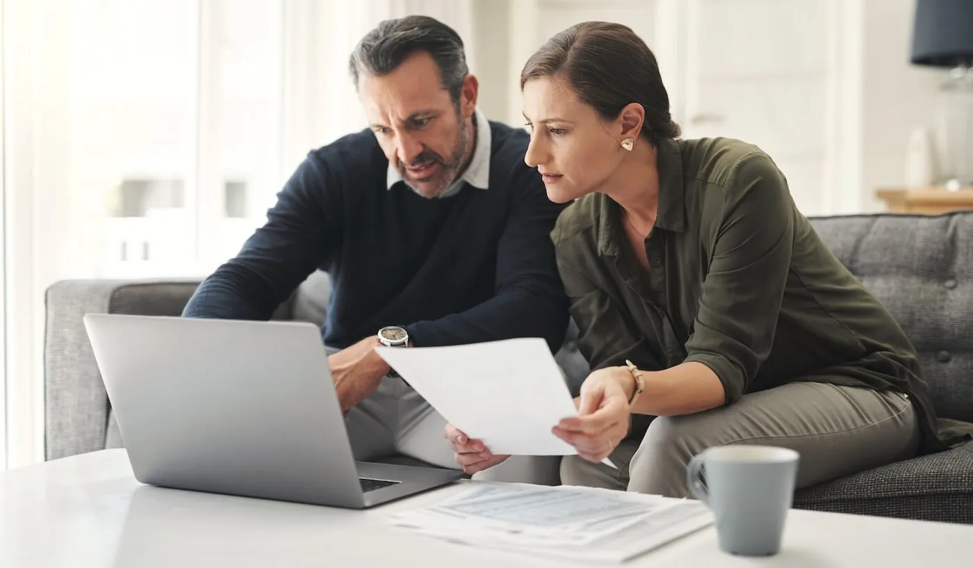 Couple reviewing printouts while checking loan options on the laptop