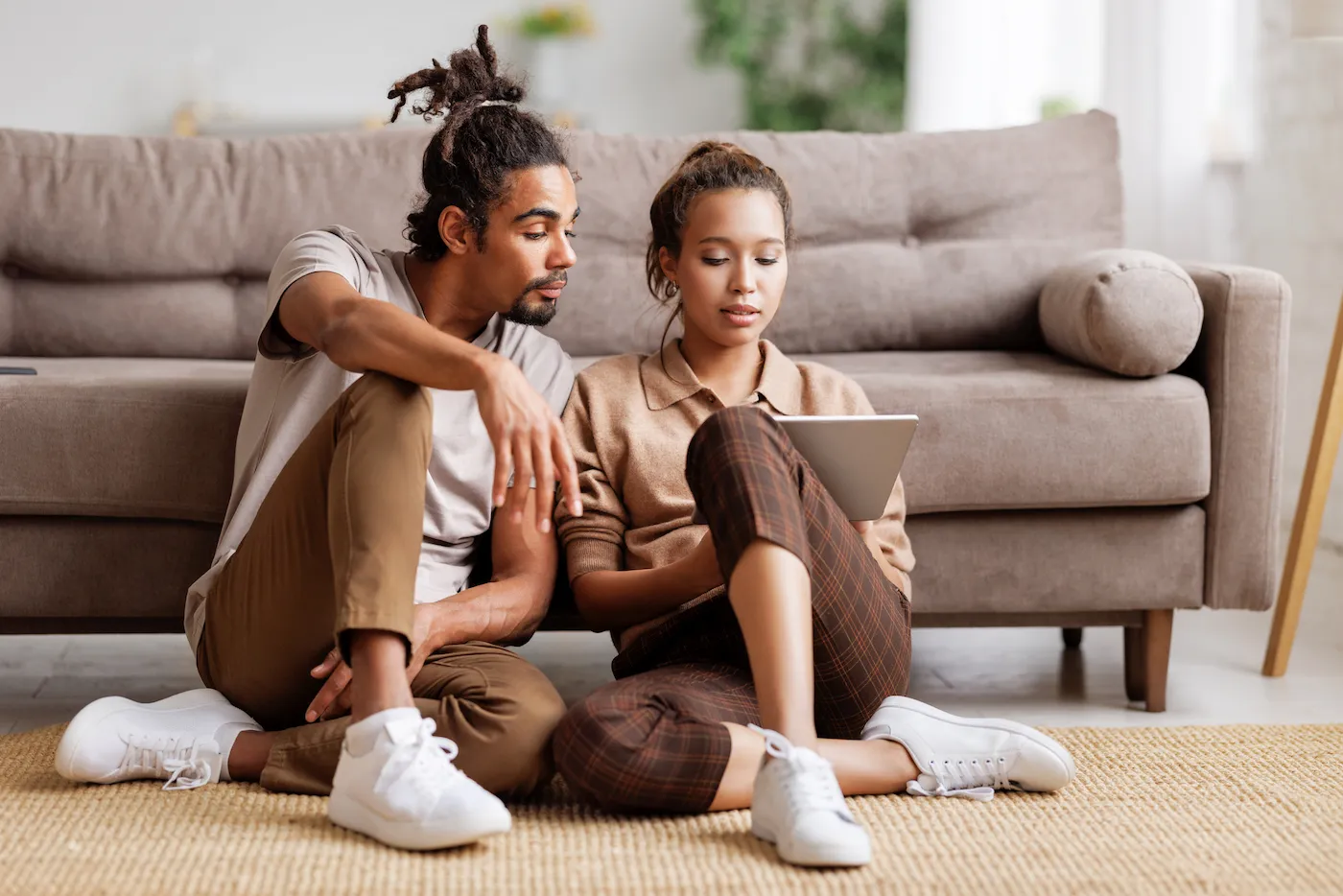 Young couple sitting on floor with digital tablet and discussing their financial future with no children