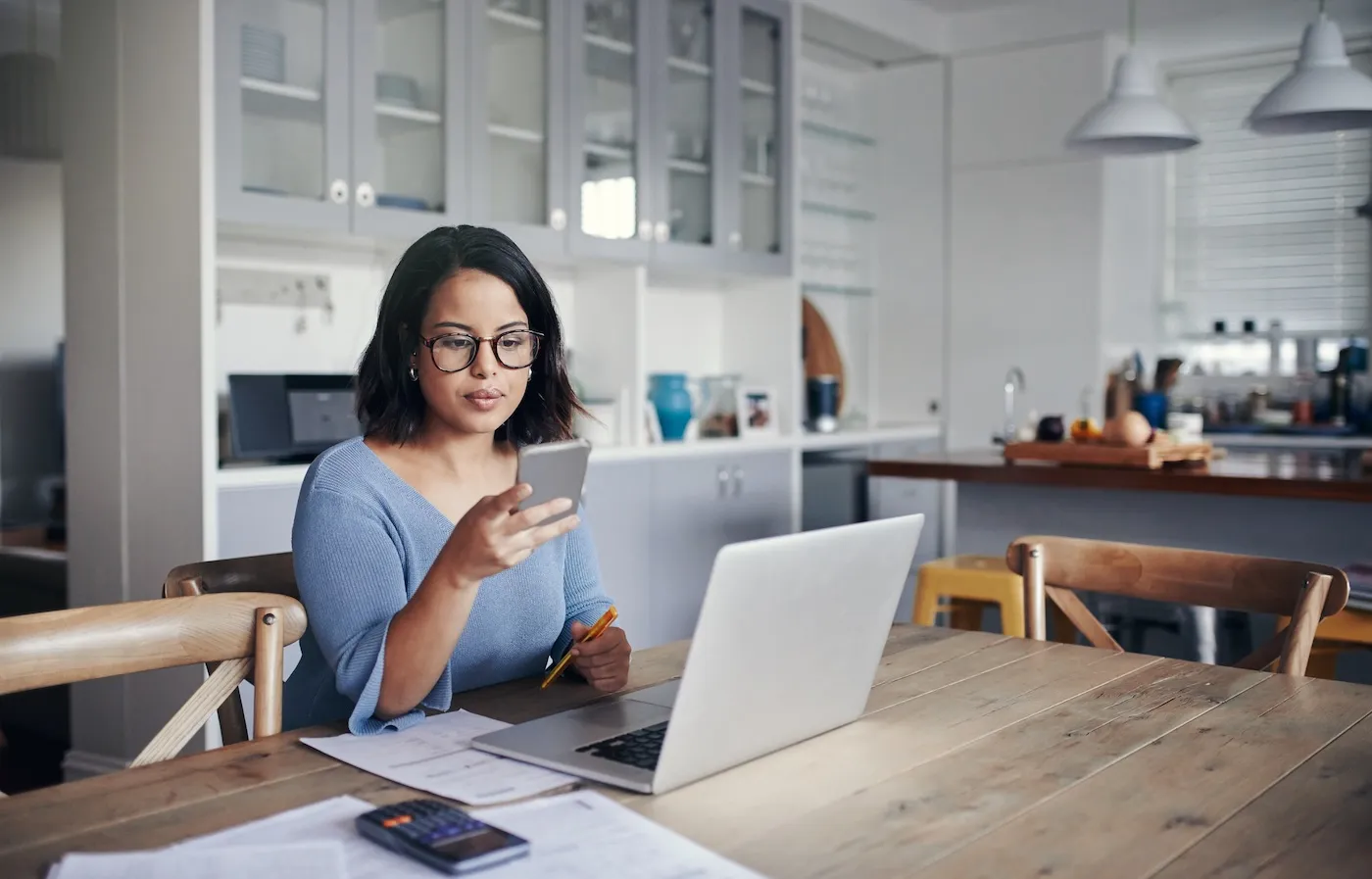 Shot of a young woman using a mobile phone and laptop while working from home.