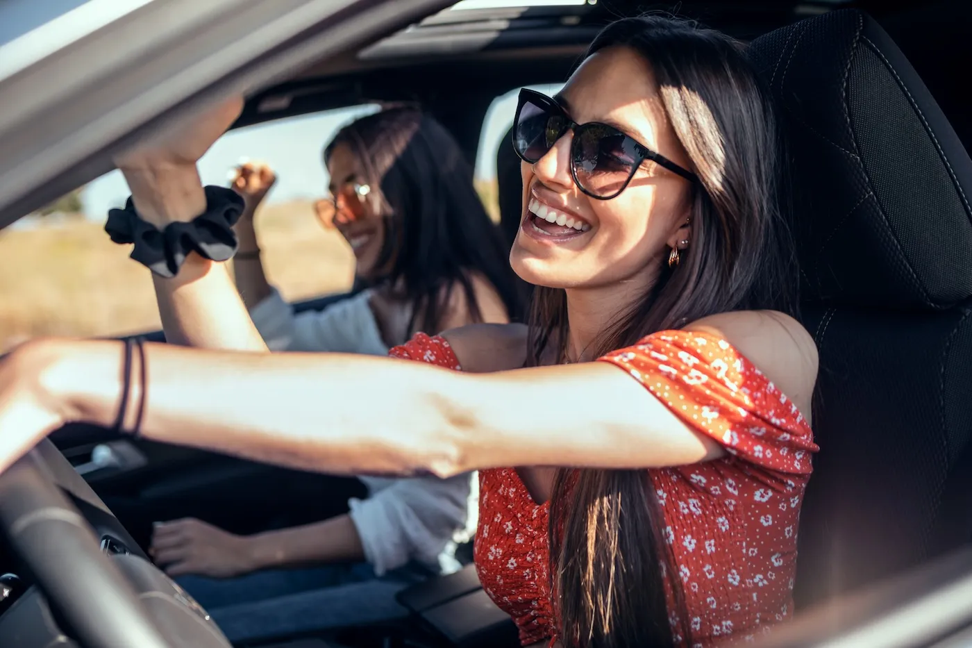 Shot of two young women singing while driving a car on road trip on beautiful summer day.