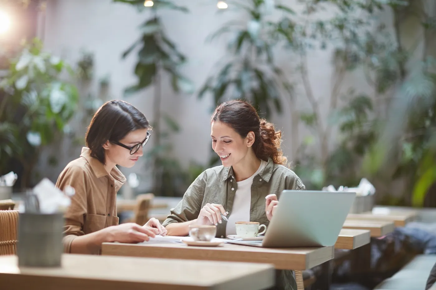 Portrait of two cheerful young women enjoying work in beautiful outdoor cafe.