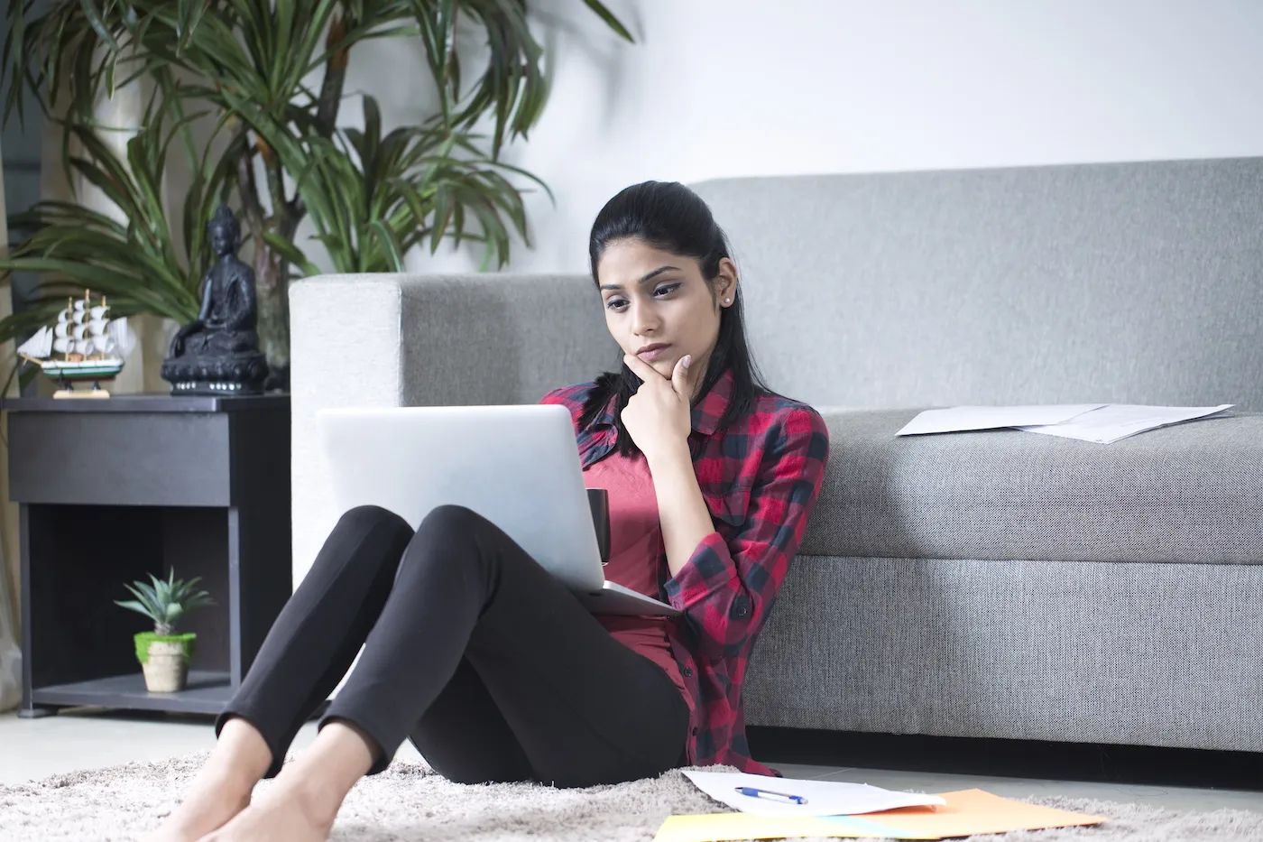 Young woman using laptop and reading documents on carpet at home
