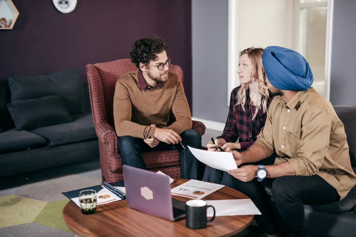 A couple asking their financial advisor about their emergency fund. They are sitting around a coffee table in their living room.