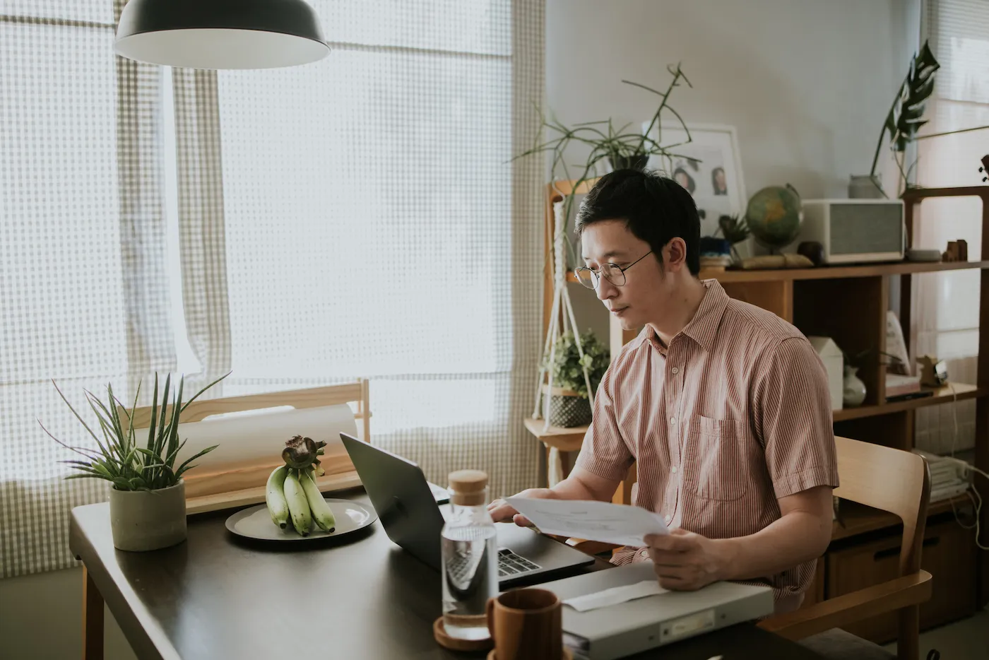 Man sitting at his kitchen table next to a large window filing taxes