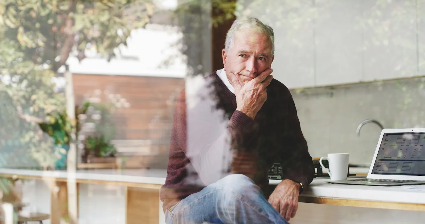 A man sitting at his desk by the window, deep in thought considering whether or not to take an early retirement package.