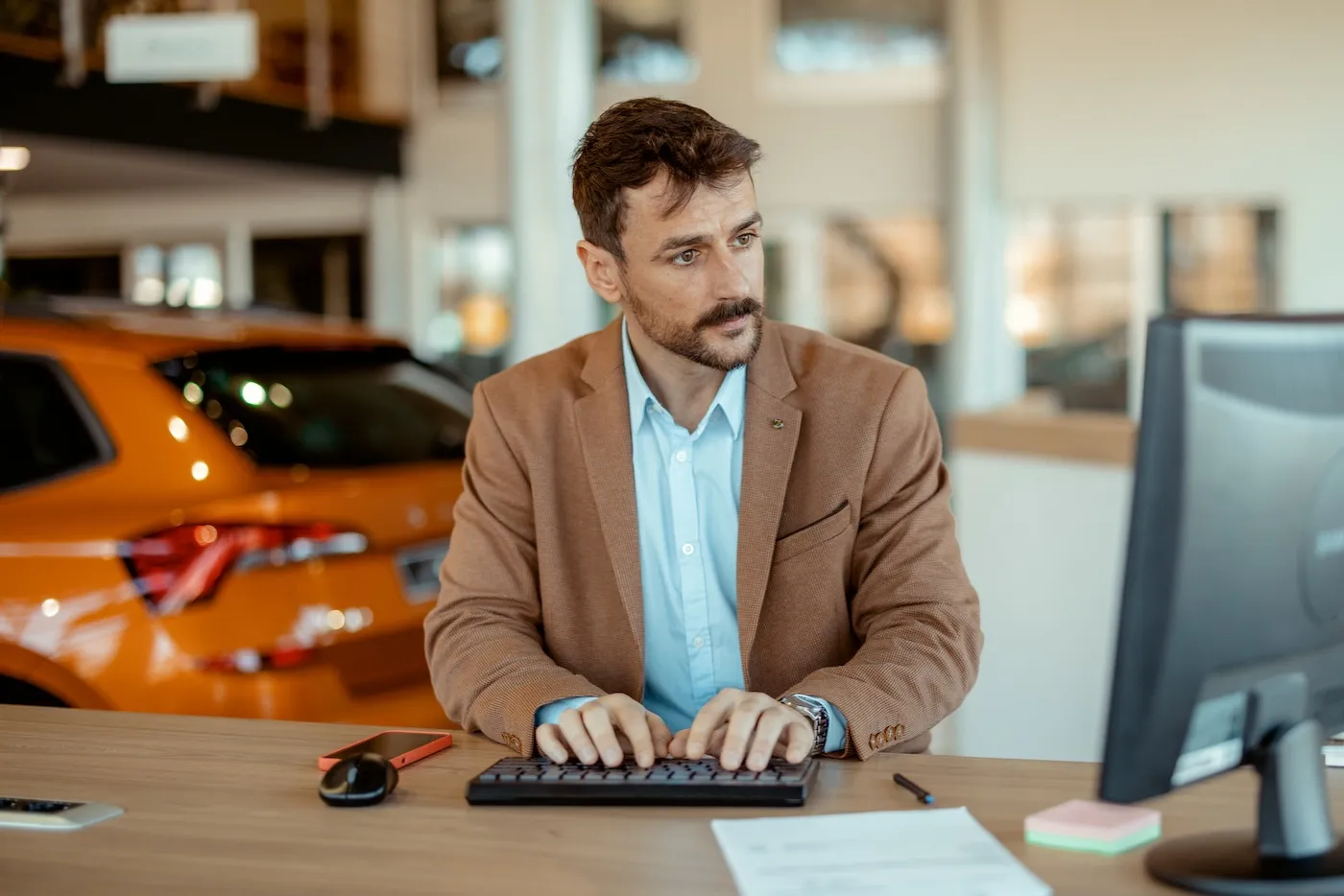 A man working on a computer in a car showroom.