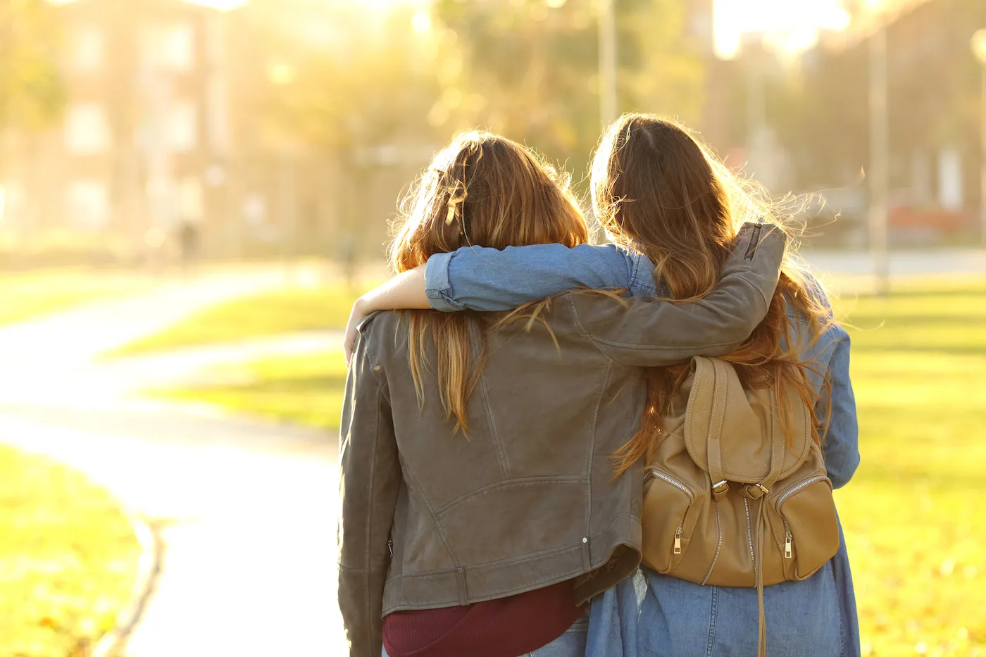 Two friends walking with one arm around the other in a sunny park.