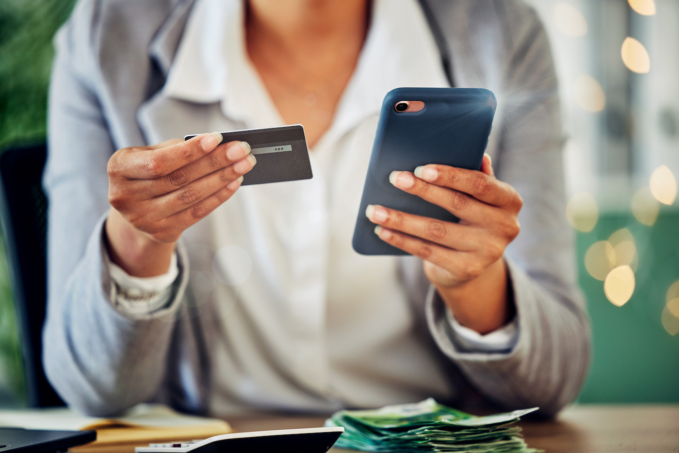 A person sitting at a table, holding a mobile phone in one hand and a credit card in the other.